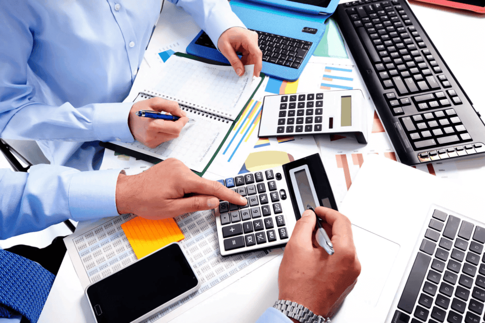 Several individuals focused on a desk, working together with a calculator and a keyboard