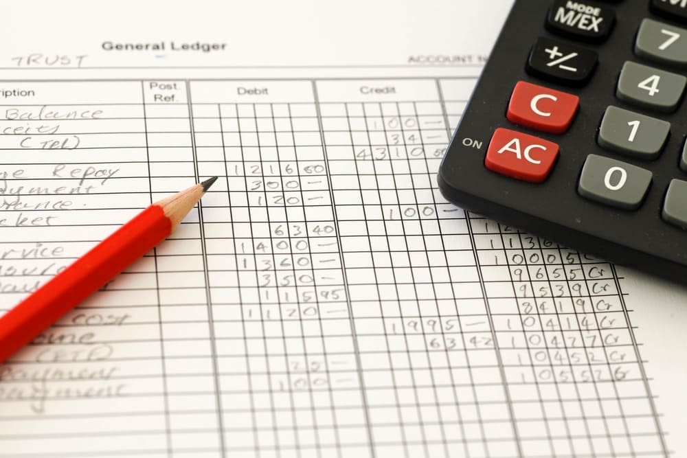 A calculator and a red pen sit on a paper with a list of expenses, ready for budgeting and financial planning